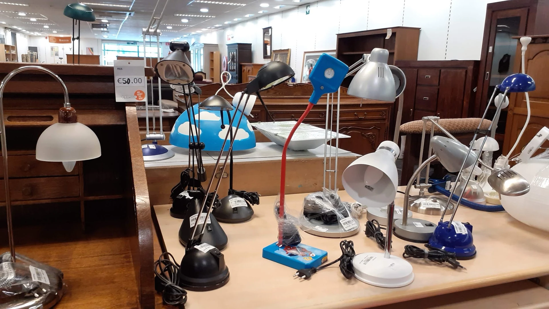 Uitgestalde tafellampjes en bureaulampen in verschillende stijlen en kleuren op een houten tafel in de winkel