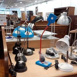 Uitgestalde tafellampjes en bureaulampen in verschillende stijlen en kleuren op een houten tafel in de winkel