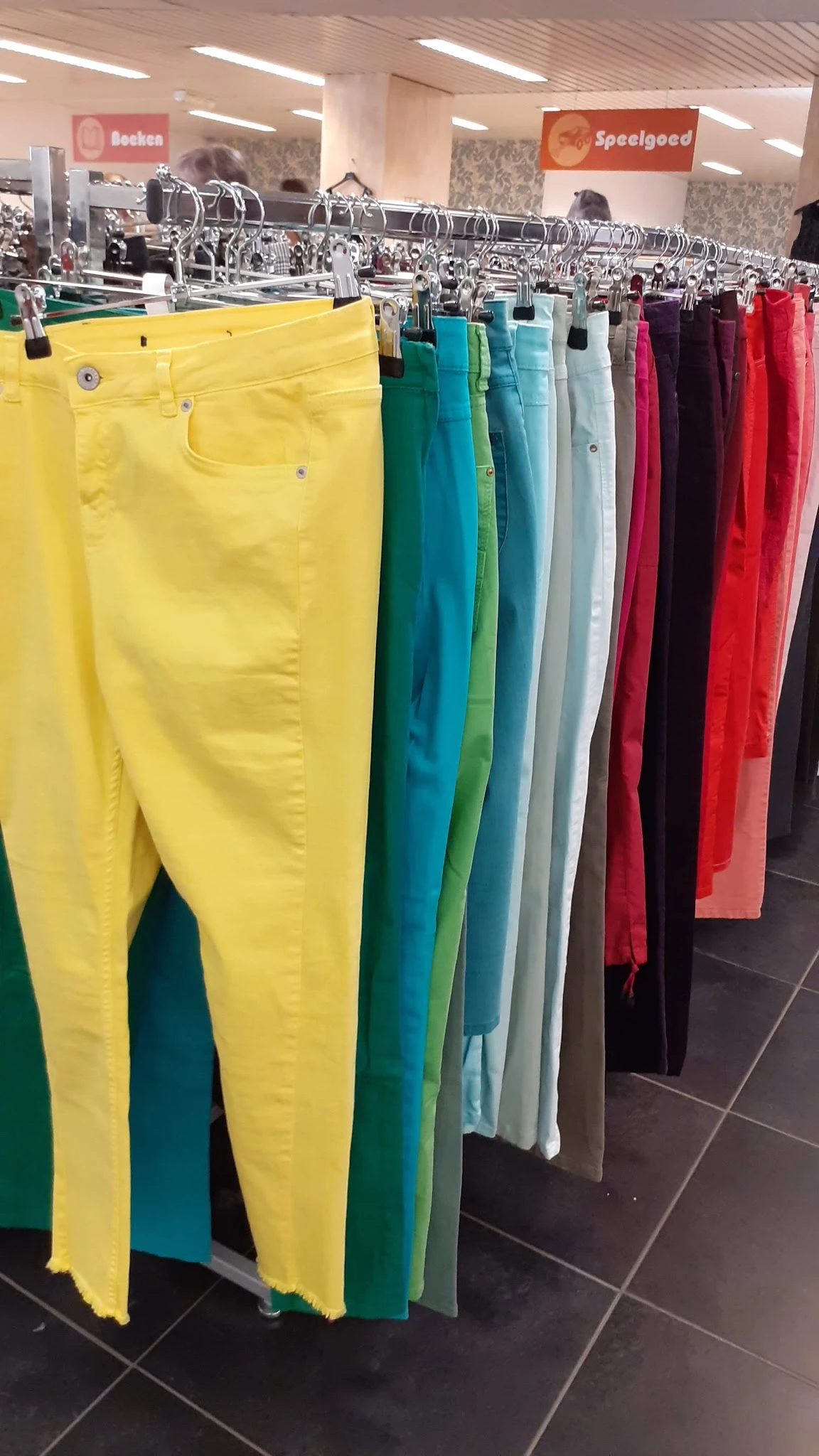 Rekken met gekleurde broeken in verschillende tinten: geel, groen, blauw, grijs, rood en zwart