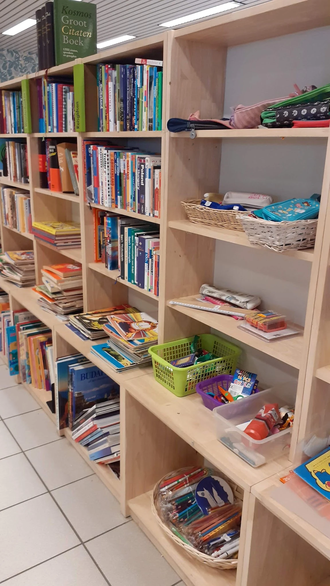 Boekenkasten met uitgestalde tweedehands boeken, tijdschriften en speelgoed in verschillende vakken en manden