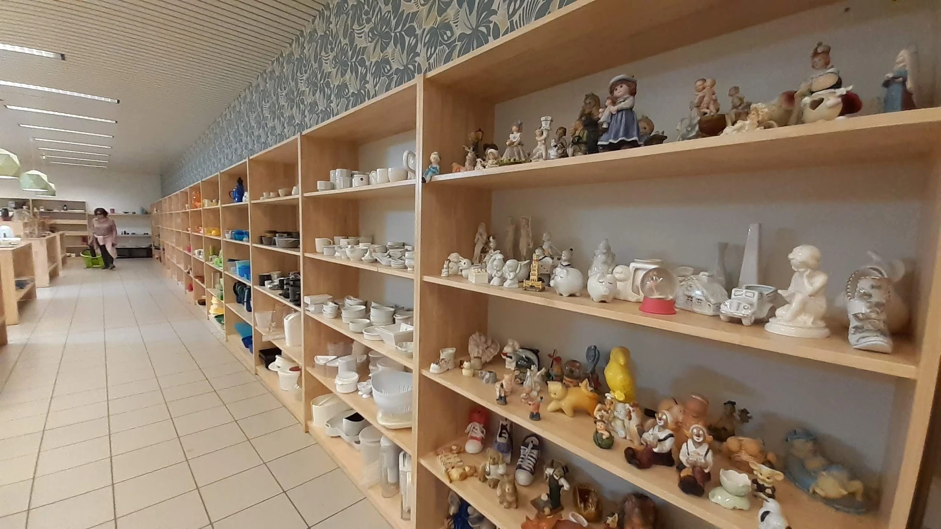 Lange rij houten stellingen met verzameling beeldjes, porselein en decoratieobjecten in een kringloopwinkel