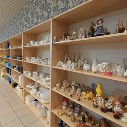 Lange rij houten stellingen met verzameling beeldjes, porselein en decoratieobjecten in een kringloopwinkel