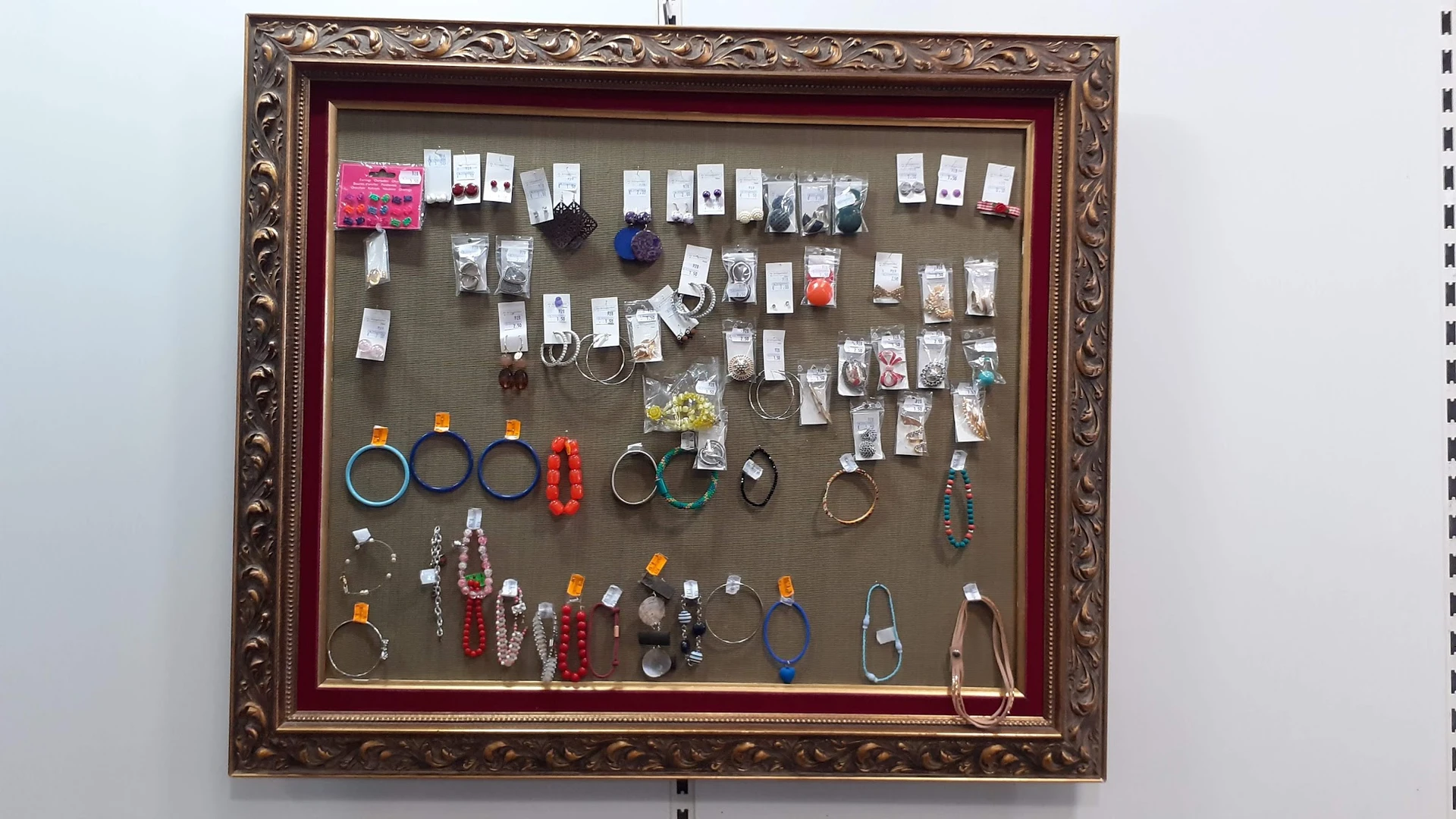 Sieradenframe met veel verschillende kettingen, ringen, armbanden en oorbellen, georganiseerd op grijs doek in goudkleurig fr