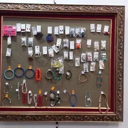 Sieradenframe met veel verschillende kettingen, ringen, armbanden en oorbellen, georganiseerd op grijs doek in goudkleurig fr