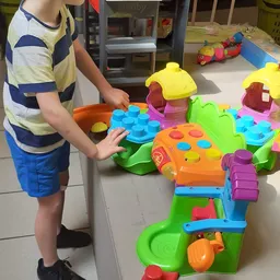 Kind speelt met kleurrijk speelgoed: huisjes en vormspeelgoed in groen, oranje en geel