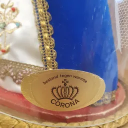 Close-up van een gele decoratieve schaal met 'Corona' opdruk en tekst 'Bestand tegen warmte'