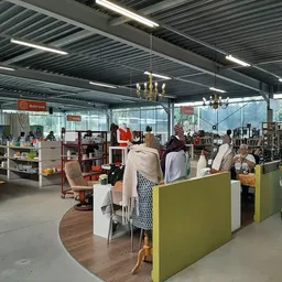 Winkelvloer van kringloopwinkel met groene scheidingswanden, boekenrekken, stellingen en bezoekers die winkelen