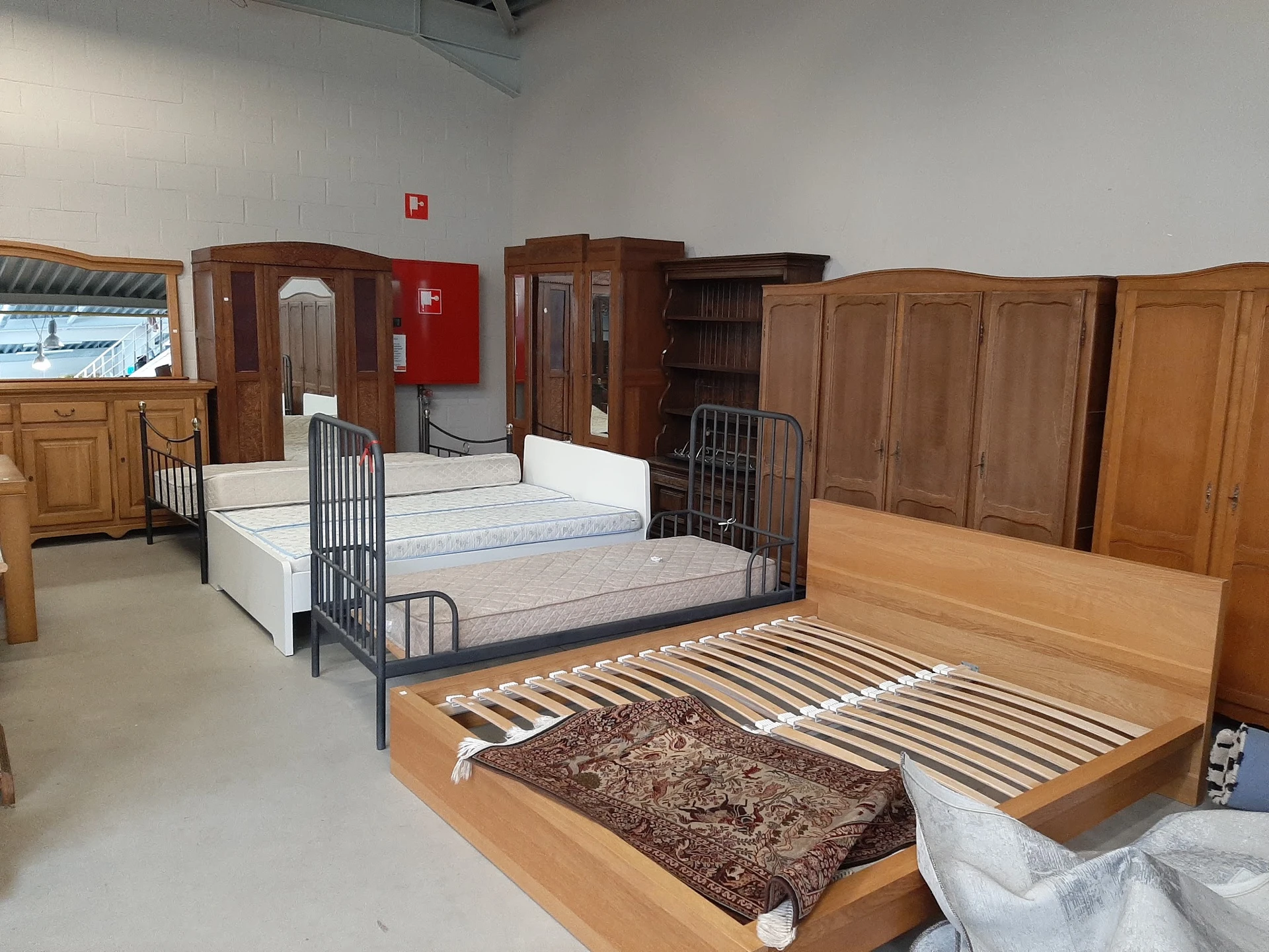 Verschillende tweedehands bedden en matrassen in de winkel, waaronder houten bedframes en metalen bedstellingen met matrassen