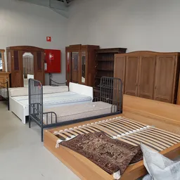 Verschillende tweedehands bedden en matrassen in de winkel, waaronder houten bedframes en metalen bedstellingen met matrassen