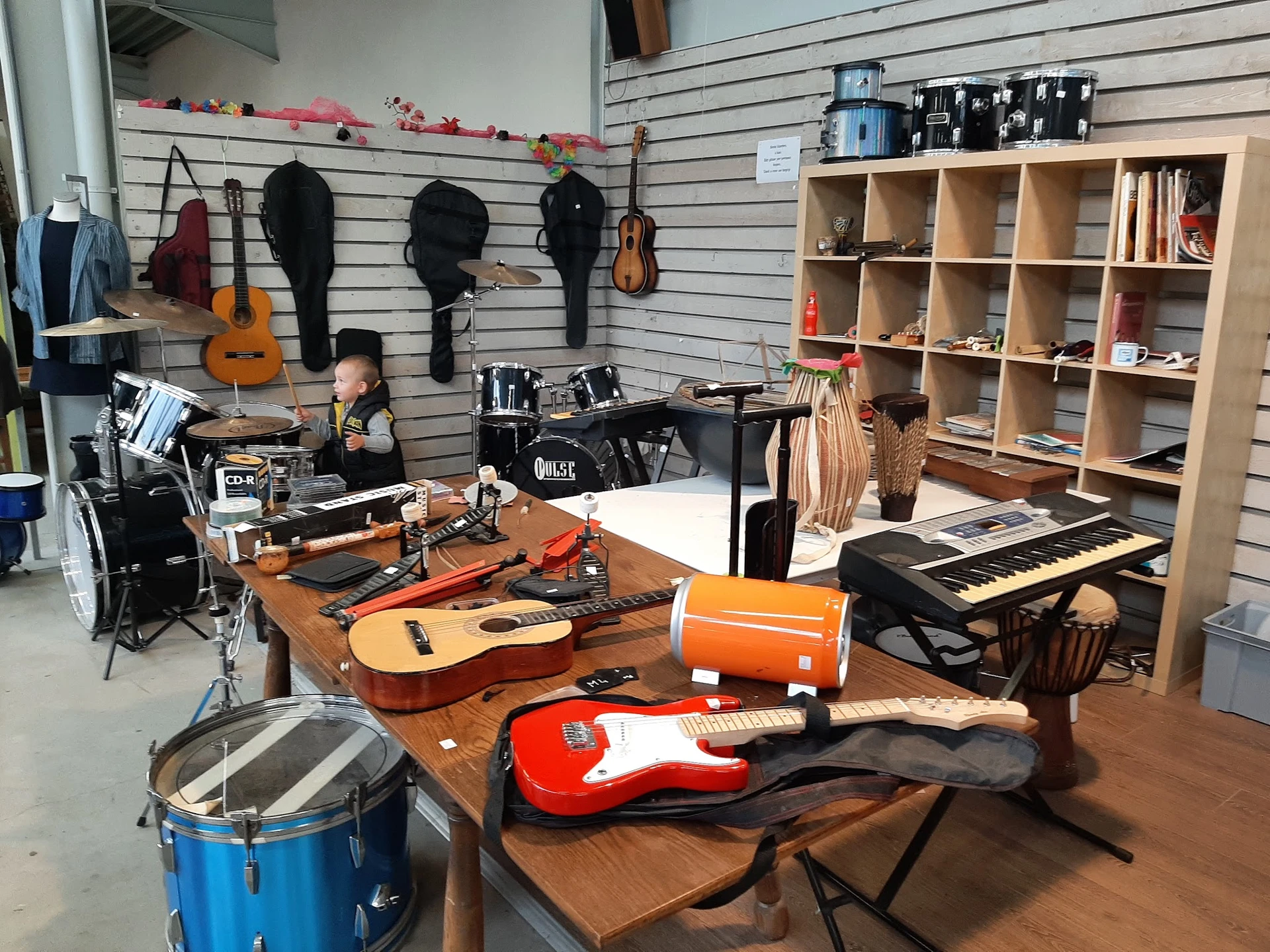 Muziekinstrumenten op houten tafel in kringloopwinkel: gitaren, drums, keyboard, orgelorgel en accessoires