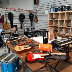 Muziekinstrumenten op houten tafel in kringloopwinkel: gitaren, drums, keyboard, orgelorgel en accessoires