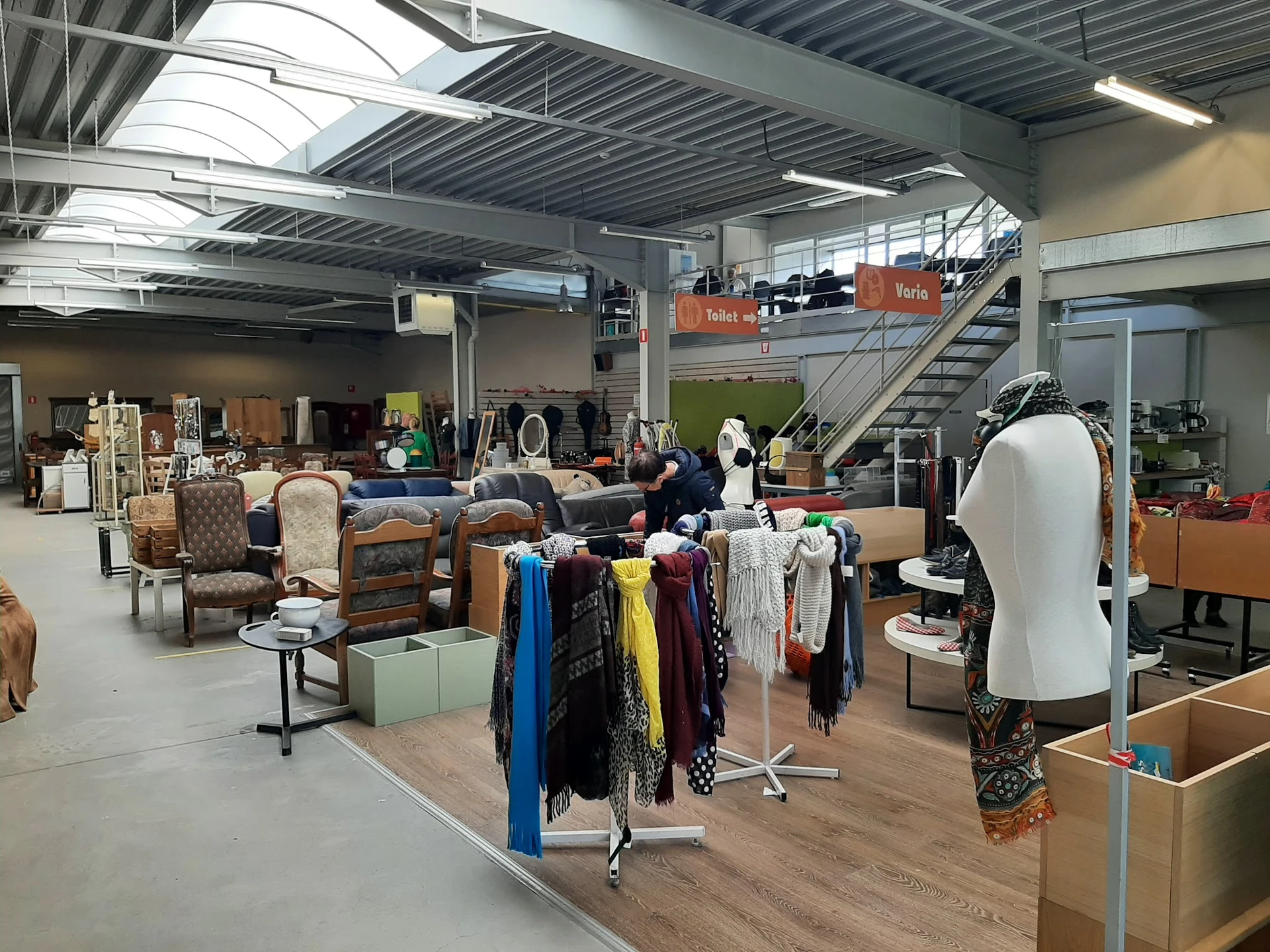 Ruim interieur van kringloopwinkel met kledingrekken, meubels, huisraad en accessoires uitgestald