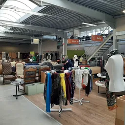 Ruim interieur van kringloopwinkel met kledingrekken, meubels, huisraad en accessoires uitgestald