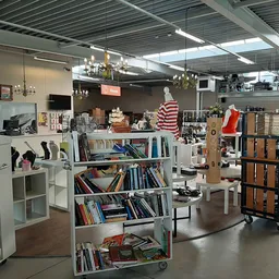 Winkelruimte met boekenkasten, displaykasten, hangende decoraties en diverse tweedehands artikelen onder industrieel plafond