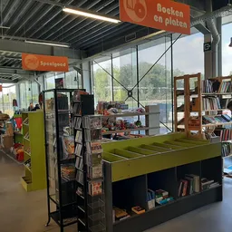 Interieur van kringloopwinkel met groene ping-pongtafel, boekenrekken en bezoekers