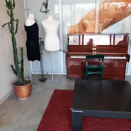 Winkelinterieur met rode piano, kledingpoppen, cactus en rode loper op betonnen vloer