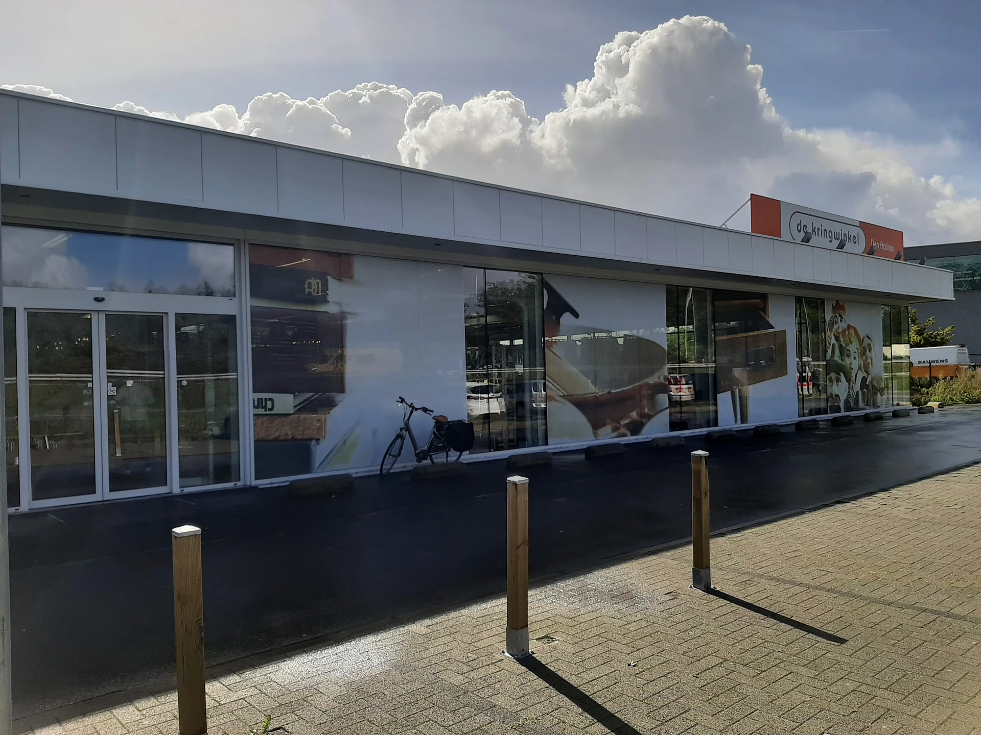 Moderne witte gevel van kringloopwinkel met glazen deuren en etalages, houten paaltjes op tegels ervoor