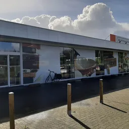 Moderne witte gevel van kringloopwinkel met glazen deuren en etalages, houten paaltjes op tegels ervoor