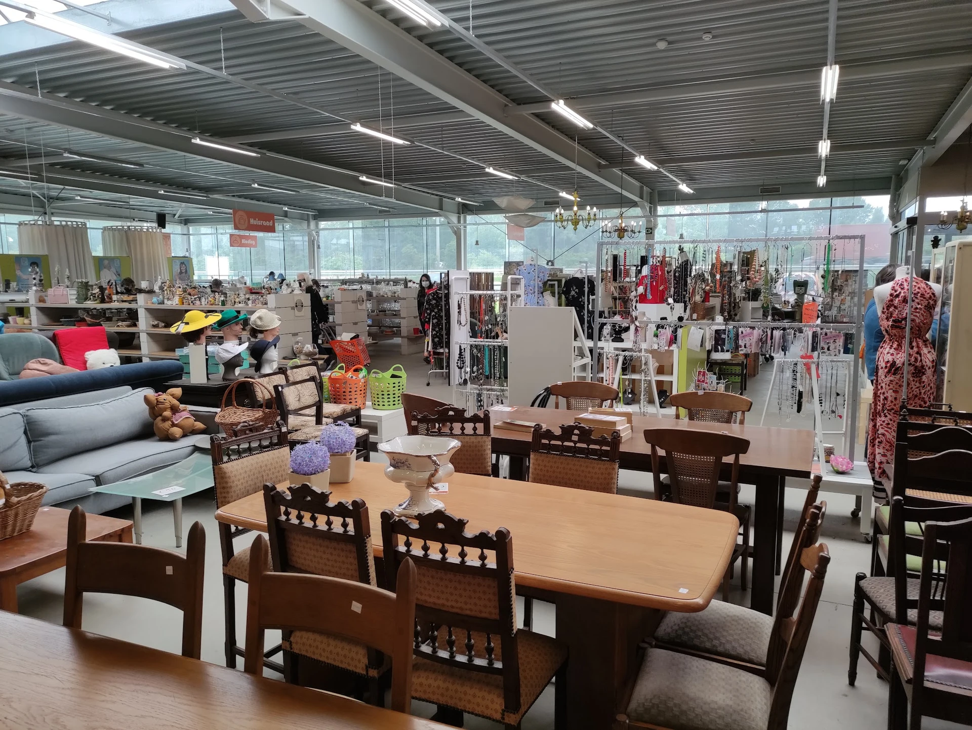 Winkelvloer met meubels, kleding aan rekken en diverse spullen in grote hal met daglicht
