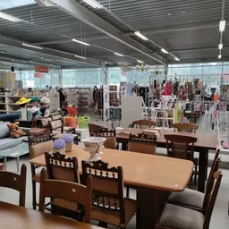 Winkelvloer met meubels, kleding aan rekken en diverse spullen in grote hal met daglicht