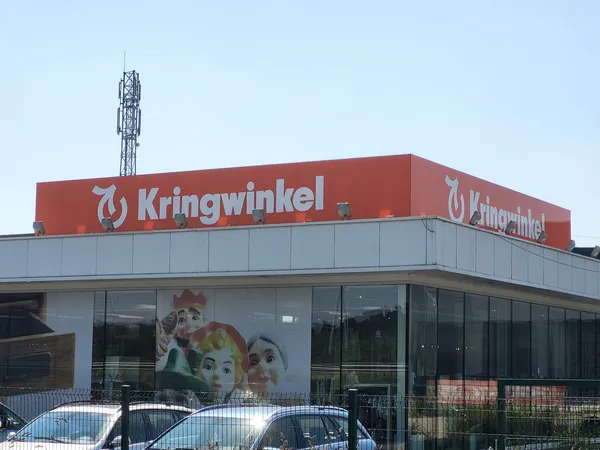 Moderne gevel van kringloopwinkel met rood logo en bord, grote ramen, parkeerplaats ervoor
