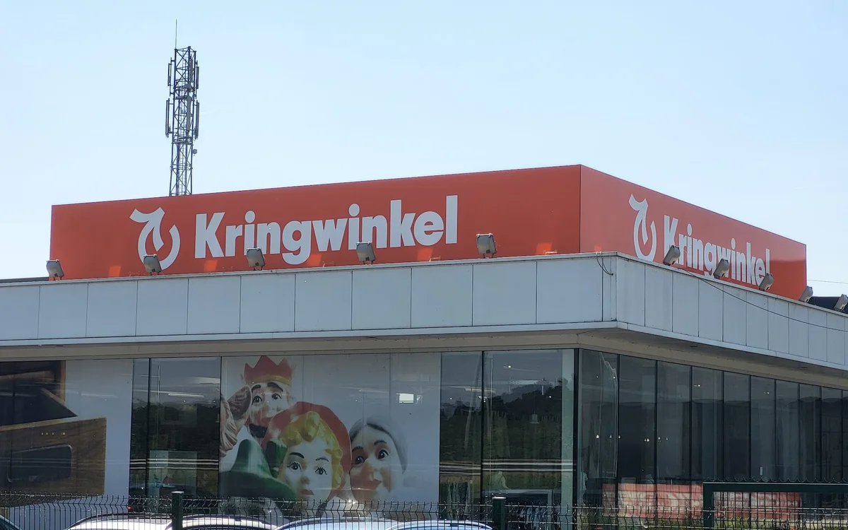 Moderne gevel van kringloopwinkel met rood logo en bord, grote ramen, parkeerplaats ervoor