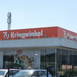Moderne gevel van kringloopwinkel met rood logo en bord, grote ramen, parkeerplaats ervoor