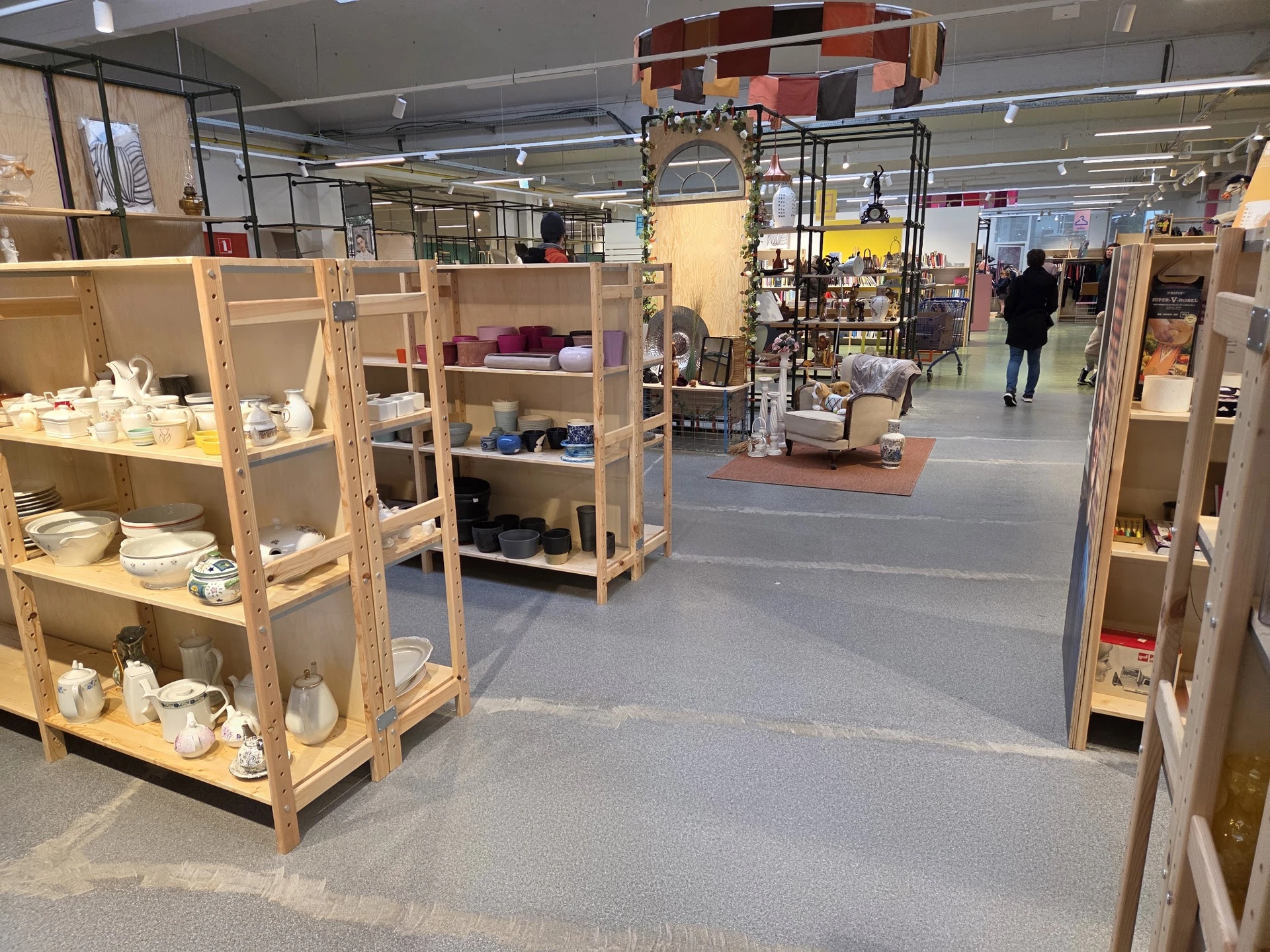 Winkelvloer met houten stellingen en vitrines vol huishoudelijke spullen in een kringloopwinkel