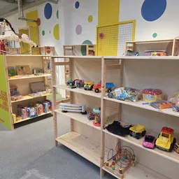 Speelgoed en kinderspullen op houten stellingen in een kringloopwinkel, met gekleurde cirkels aan het plafond