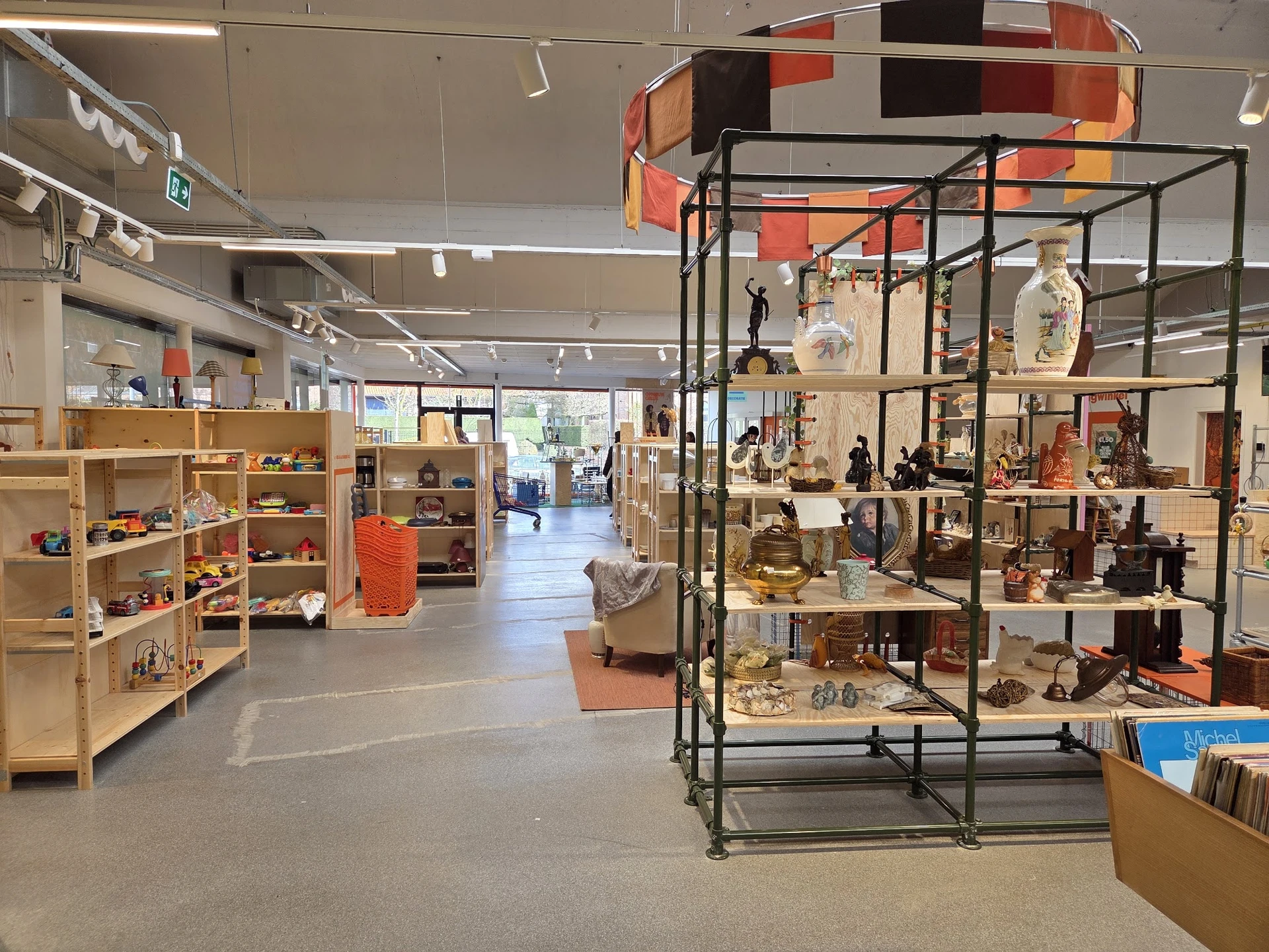 Overzicht van kringloopwinkelzaal met stellingen, vitrines en uitgestalde artikelen op meerdere niveaus