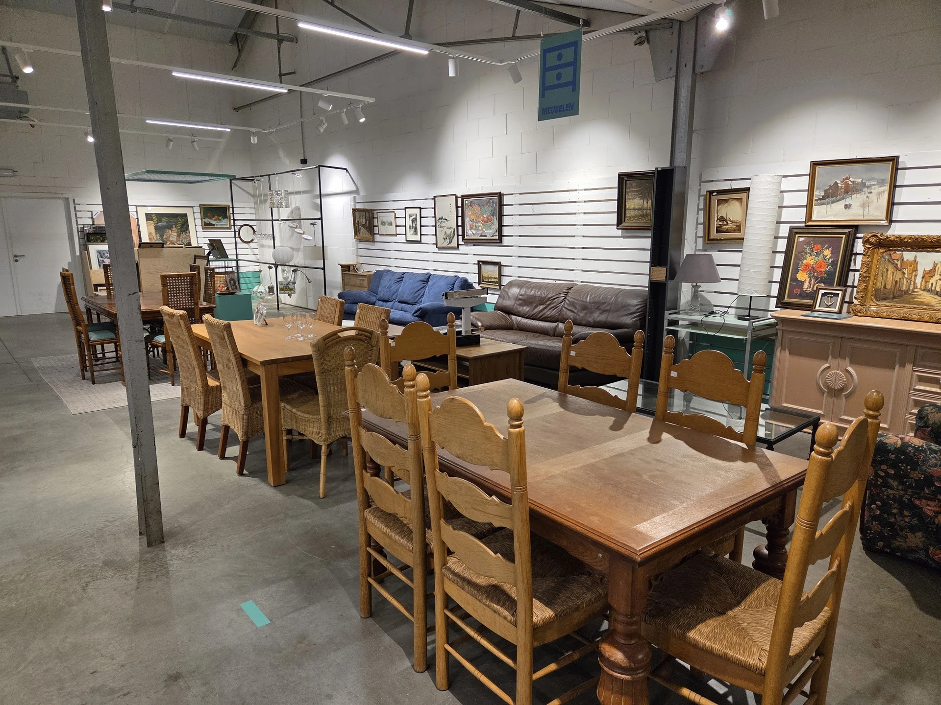 Winkelvloer met houten eettafels, stoelen, kasten en schilderijen aan de muur