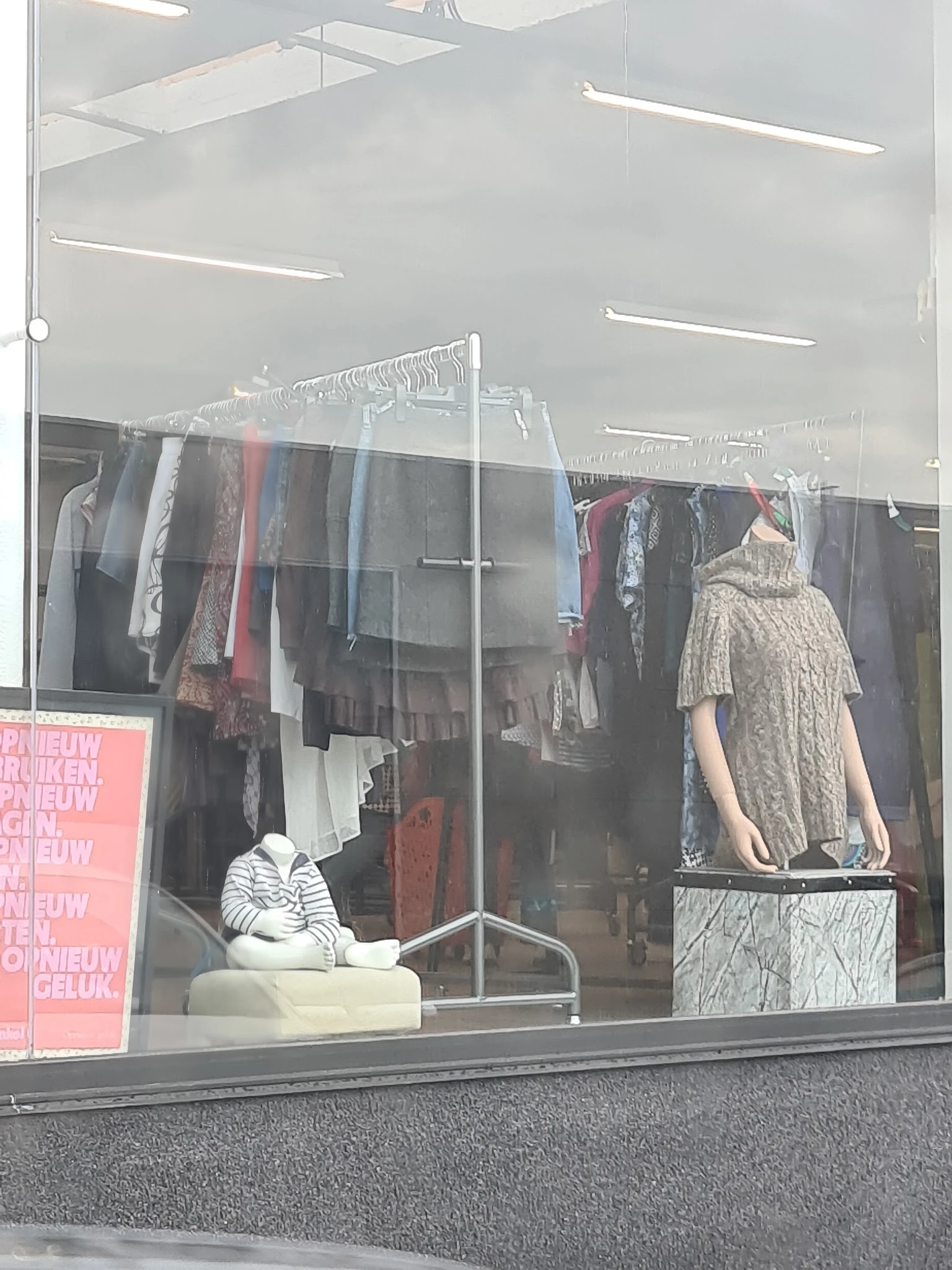 Rekken met tweedehands kleding aan hangers in een kringloopwinkel, met een mannequin in beige jurk
