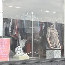 Rekken met tweedehands kleding aan hangers in een kringloopwinkel, met een mannequin in beige jurk