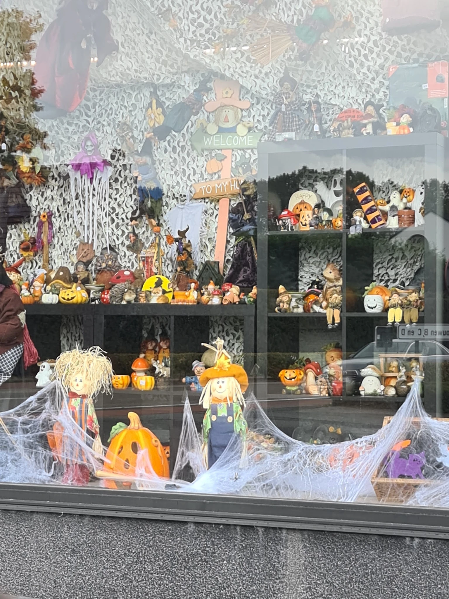Etalage met Halloween-decoraties: pompoenen, skeletten, spinnenweb en diverse seizoensversieringen achter glas