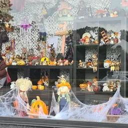 Etalage met Halloween-decoraties: pompoenen, skeletten, spinnenweb en diverse seizoensversieringen achter glas