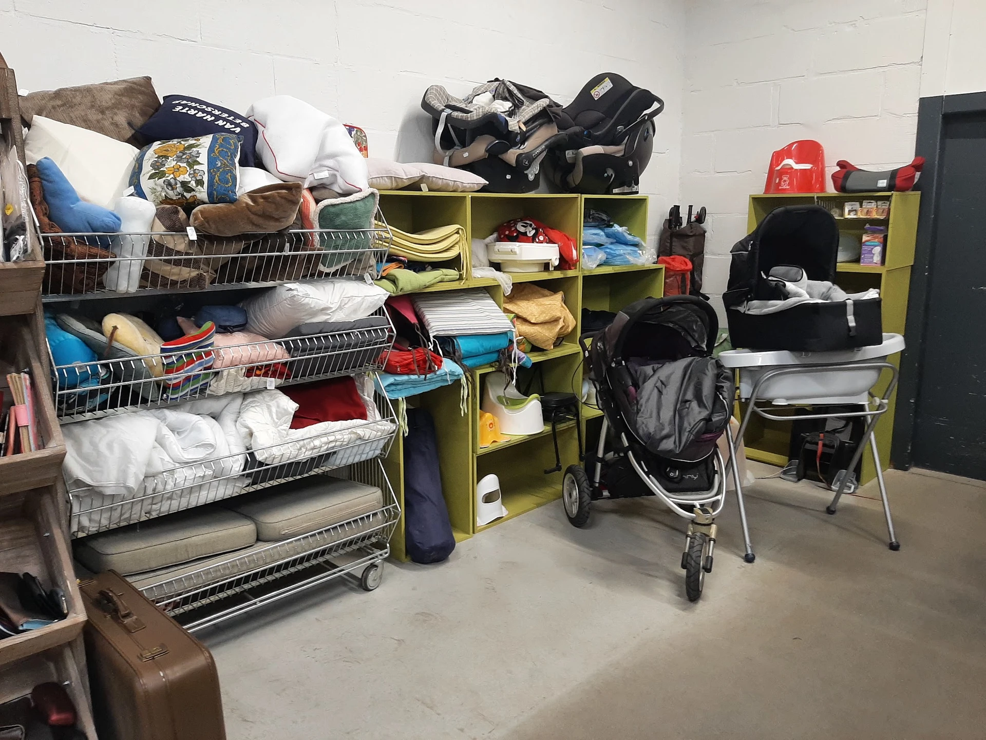 Opbergruimte met winkelrekken vol met kleding, huishoudartikelen, een kinderwagen en diverse gebruikte spullen