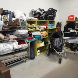 Opbergruimte met winkelrekken vol met kleding, huishoudartikelen, een kinderwagen en diverse gebruikte spullen