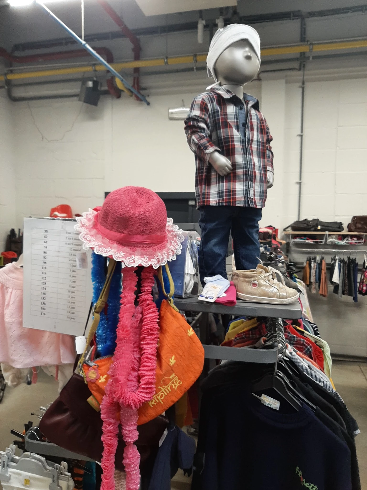 Tweedehands kleding en accessoires op toonbank, inclusief roze hoed, gekleurde sjaals en schoenen