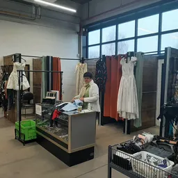Winkelvloer met kledingrekken, een toonbank en een medewerker die goederen sorteert