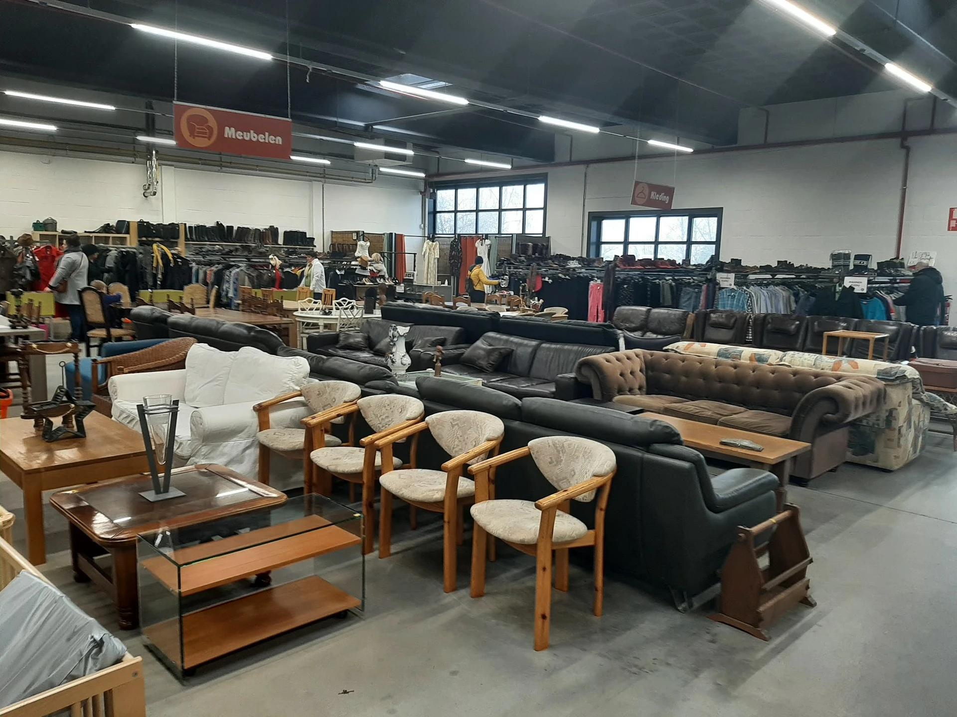 Showroomvloer met tweedehands meubels: banken, fauteuils, salontafels en stoelen uitgestald in een groot pand met fluorescent
