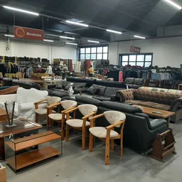 Showroomvloer met tweedehands meubels: banken, fauteuils, salontafels en stoelen uitgestald in een groot pand met fluorescent