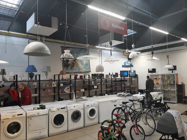 Winkelvloer met wasmachines, fietsen en stellingen vol spullen onder industriële verlichting