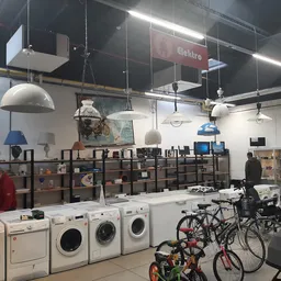 Winkelvloer met wasmachines, fietsen en stellingen vol spullen onder industriële verlichting