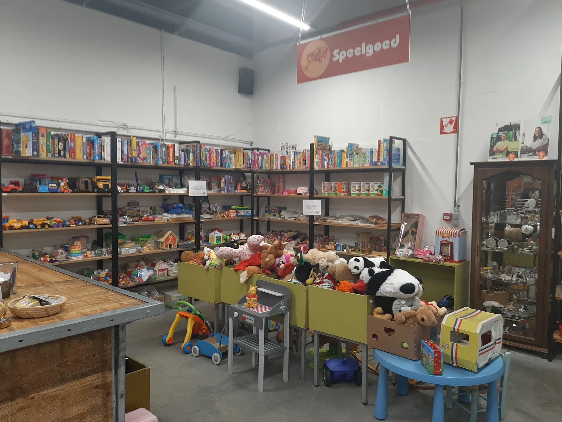 Speelgoedafdeling met kinderspeelgoed in bakken, stellingen met bordspellen en actiefiguren op de achtergrond