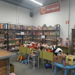Speelgoedafdeling met kinderspeelgoed in bakken, stellingen met bordspellen en actiefiguren op de achtergrond