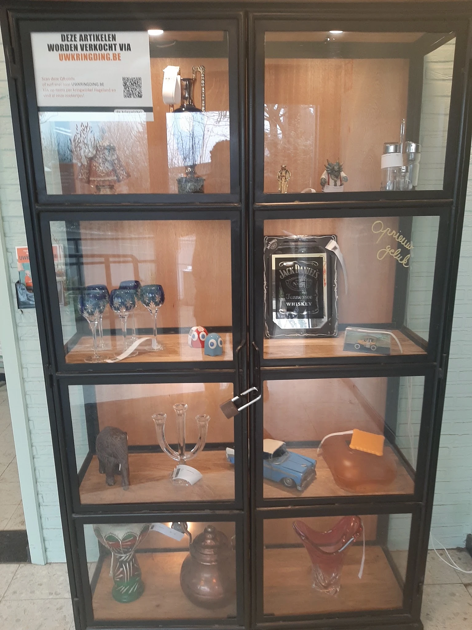 Glazen vitrinekast met tweedehands items: glazen, Jack Daniel's-merchandising, decoratieve spullen en accessoires