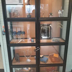 Glazen vitrinekast met tweedehands items: glazen, Jack Daniel's-merchandising, decoratieve spullen en accessoires