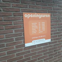 Oranje bord met openingstijden van een winkel op een bakstenen muur