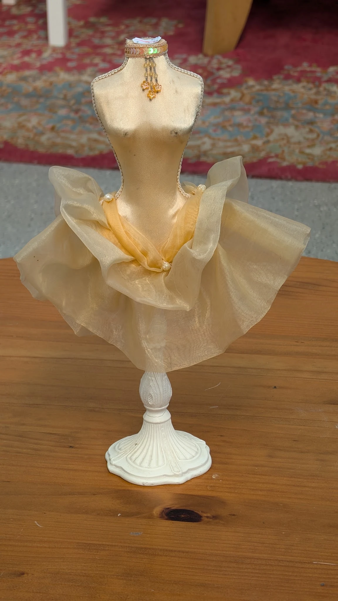 Decoratieve pop met doorschijnend geel en wit kledingstuk op houten voet