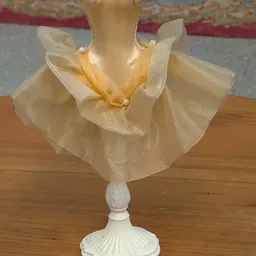 Decoratieve pop met doorschijnend geel en wit kledingstuk op houten voet